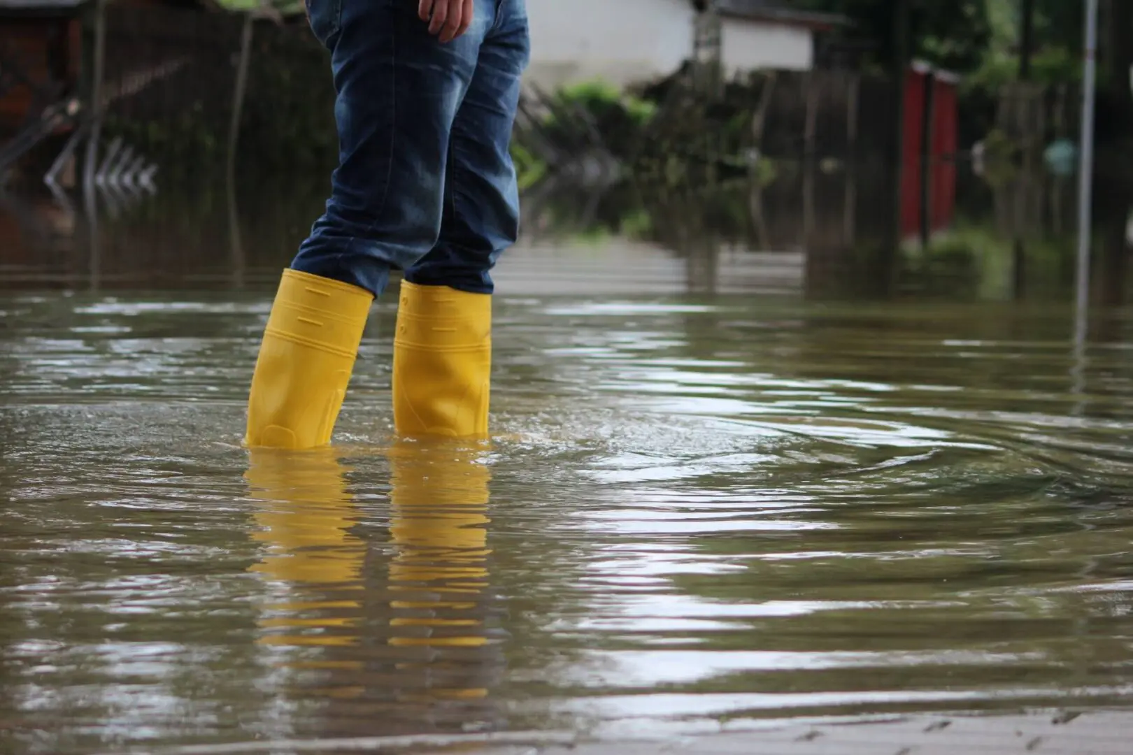 Person wearing yellow boots stands in knee-high floodwater on a street.